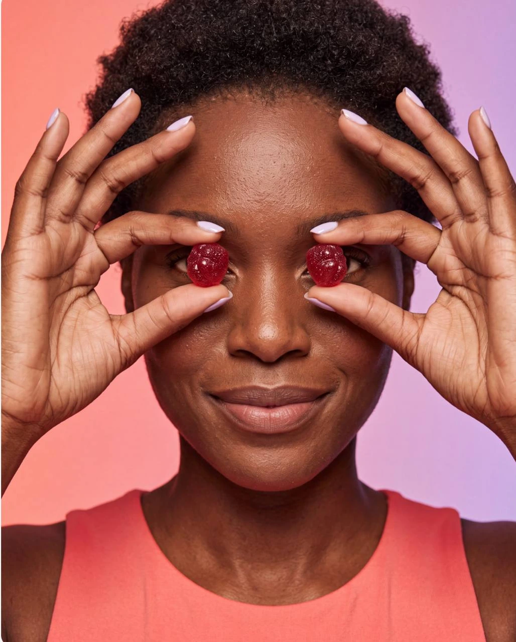 Black woman holding two red gummies over her eyes